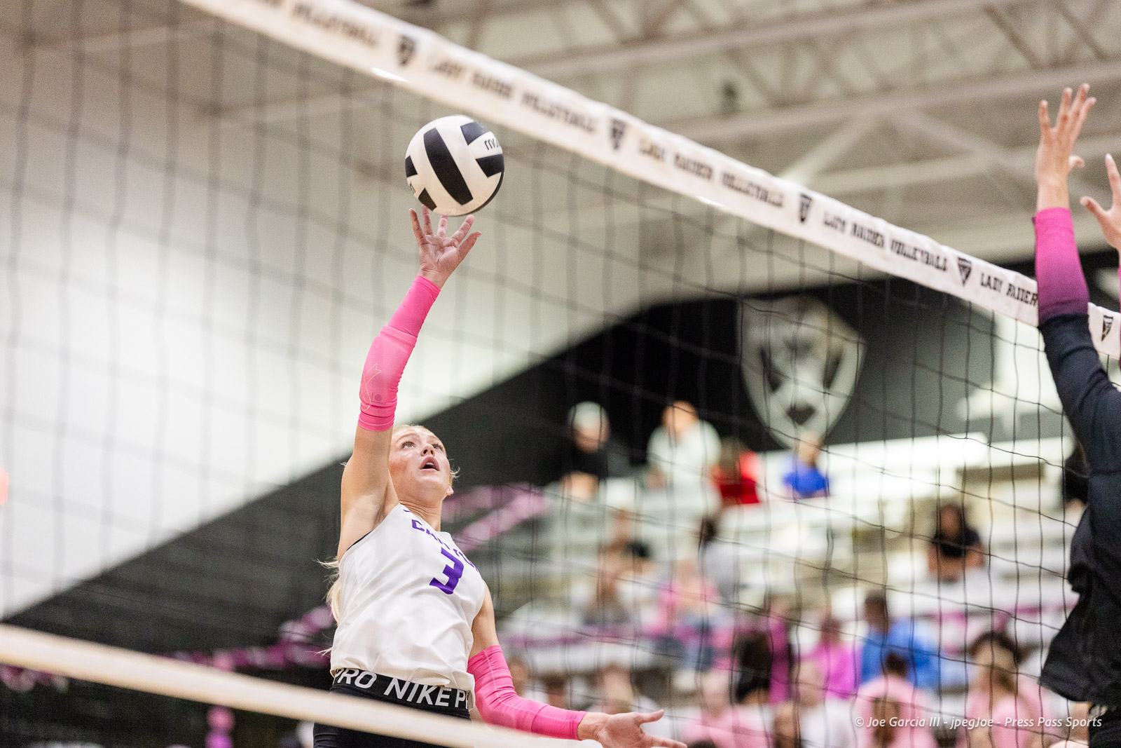 canyon-vs-west-plains-2026-25 | Press Pass Sports Female volleyball player in white and pink reaches to spike the ball over the net.