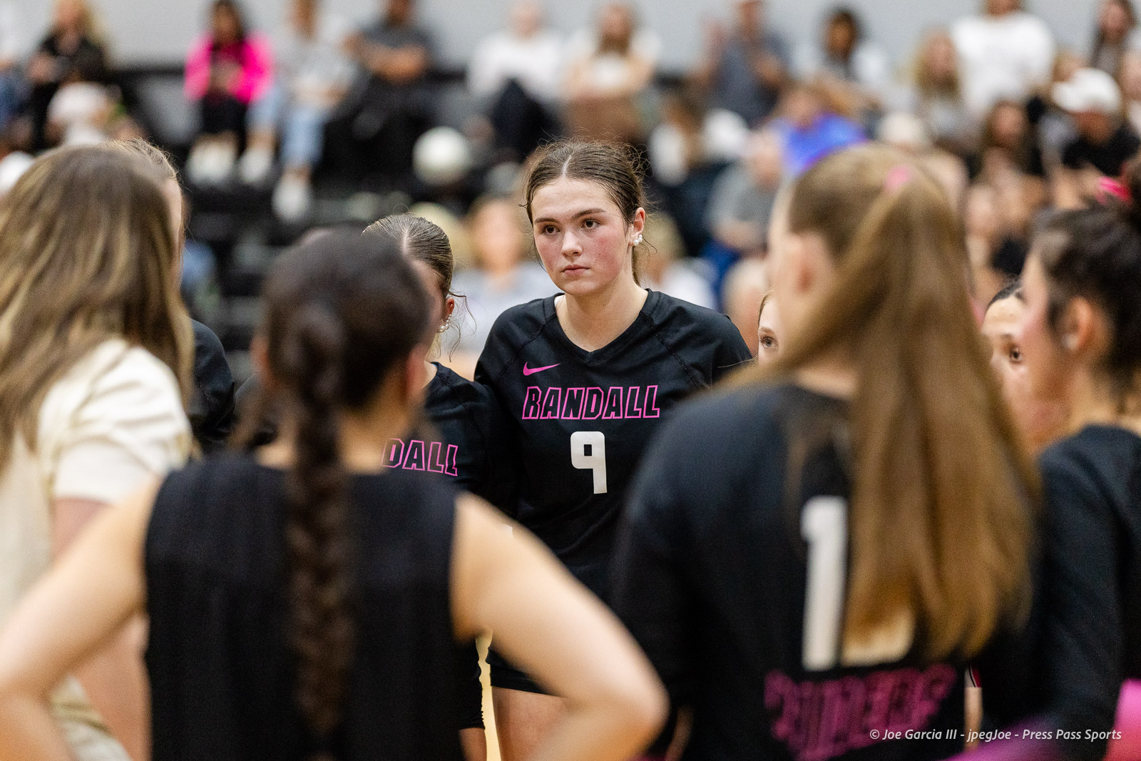 canyon-vs-west-plains-2026-32 | Press Pass Sports Close-up of a female volleyball player wearing a black Randall jersey with the number 9, standing in a huddle with teammates.