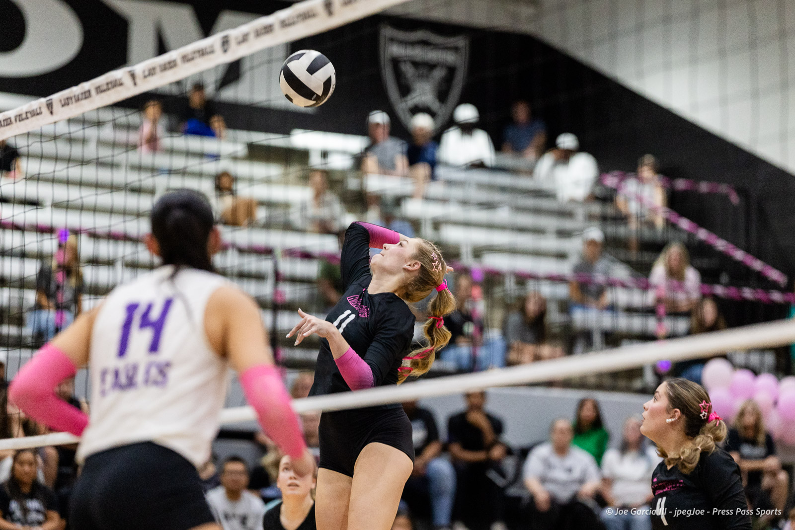 canyon-vs-west-plains-2026-36 | Press Pass Sports Female volleyball player in a black uniform (number 11) spikes the ball over the net, with teammates and spectators in the gym behind.