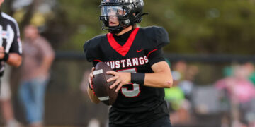 Football player in a black and red Mustangs uniform runs with the ball during a game.