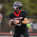 Football player in a black and red Mustangs uniform runs with the ball during a game.
