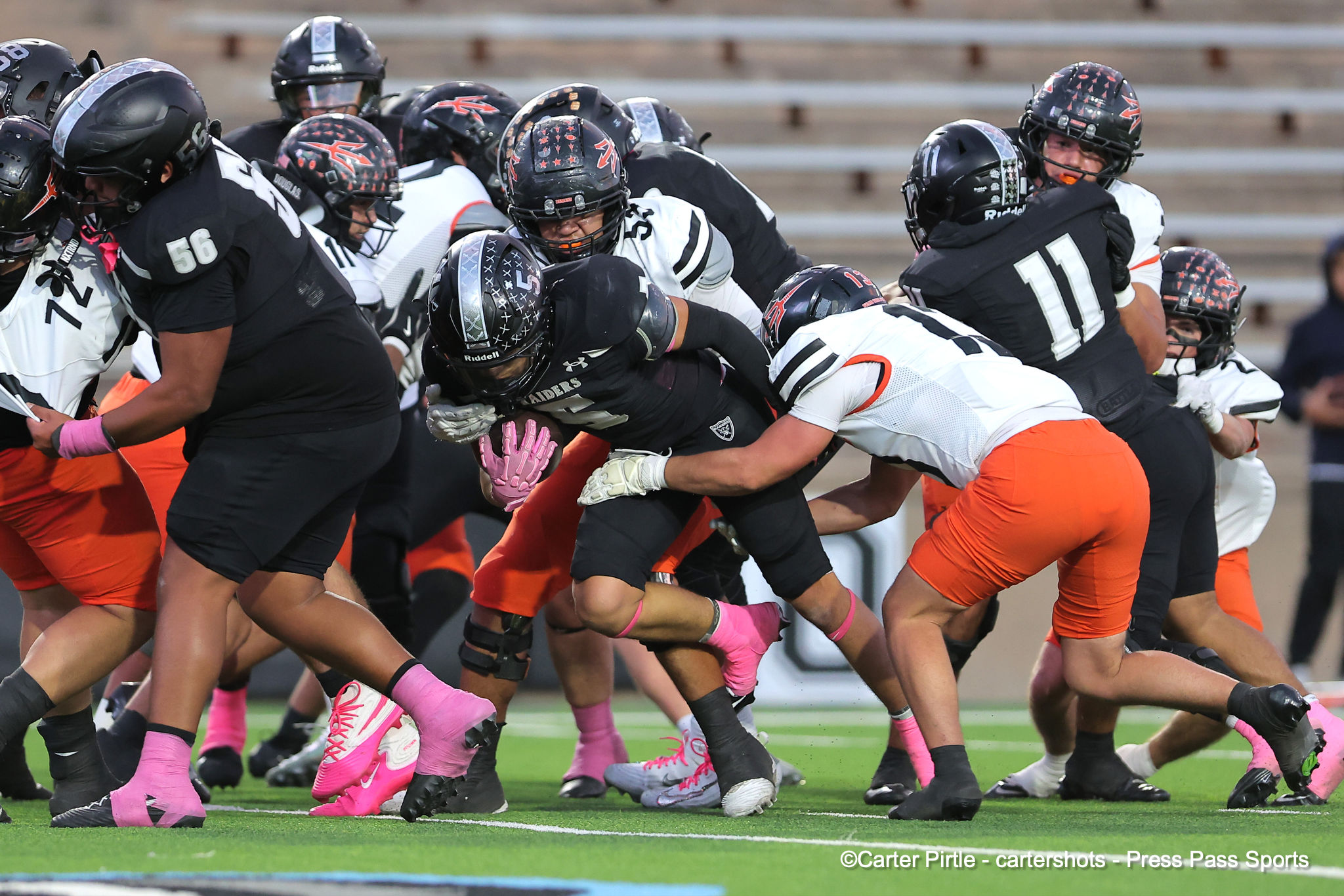 Tackle pile of football players in black and white jerseys colliding on a green field, pink socks and shoes visible in foreground
