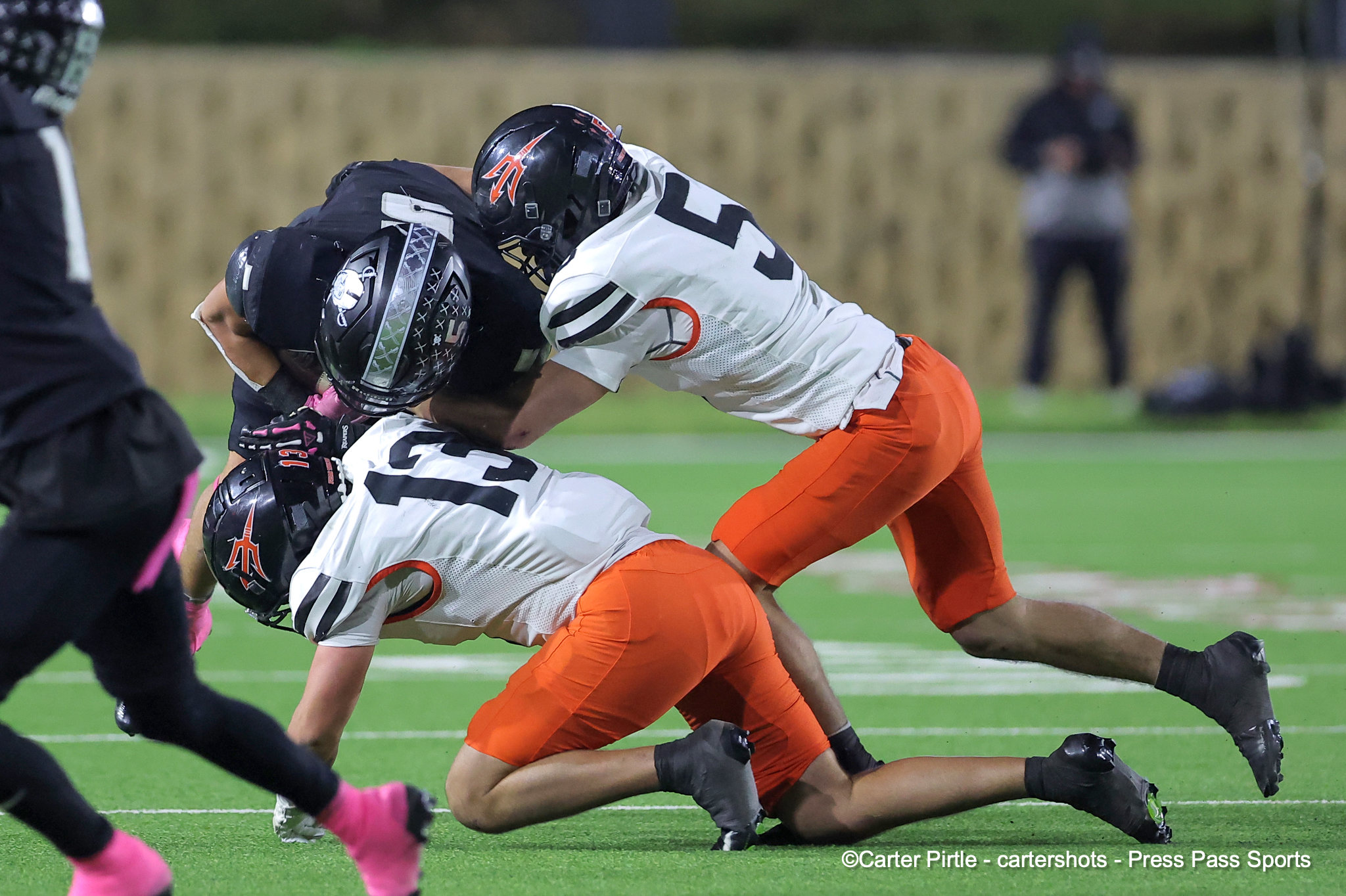Two football players collide in a tackle on a green field during a game, one in white/orange and the other in dark colors with helmets.