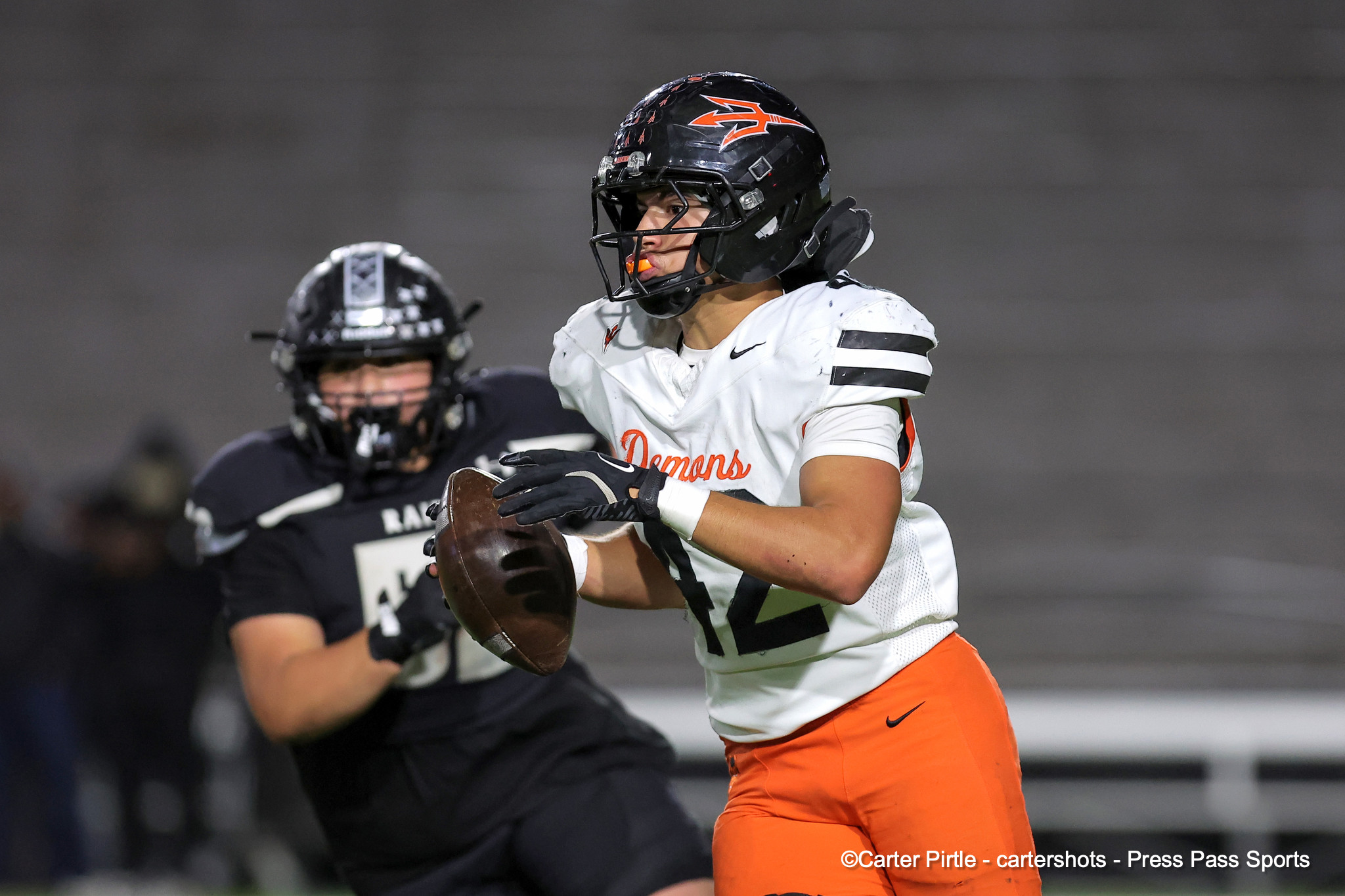 Football player in white jersey reaching for a catch, orange pants, black helmet with red logo, on a night game field