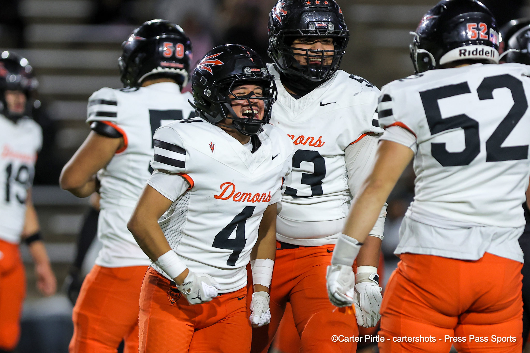 Group of football players in white jerseys with orange pants celebrating on the field.