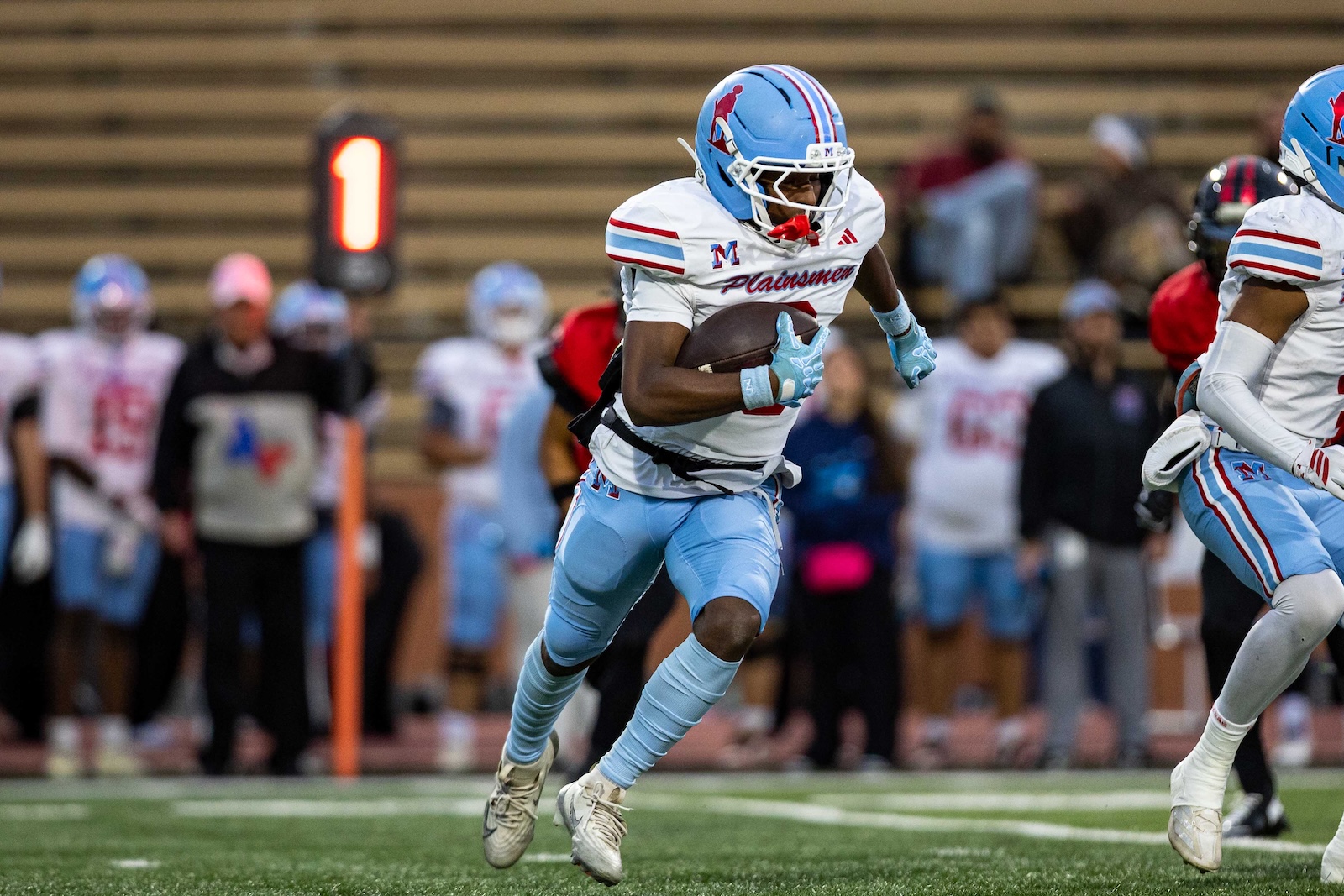 MHS-THS-FB-8 | Press Pass Sports Football player in light blue and white uniform runs with the ball during a game, crowd in the background.