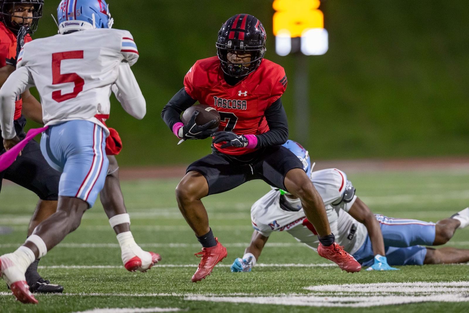 MHS-THS-FB-12 | Press Pass Sports Football player in red Tascola jersey running with ball, pursued by opponents on a grassy field at night