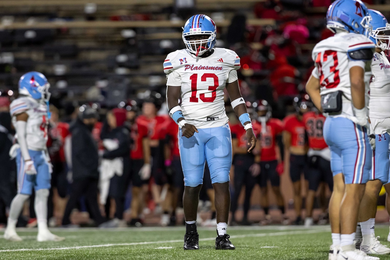 MHS-THS-FB-26 | Press Pass Sports Football player wearing number 13 in a white Plainsmen jersey and light blue pants stands on the field with teammates in the background.