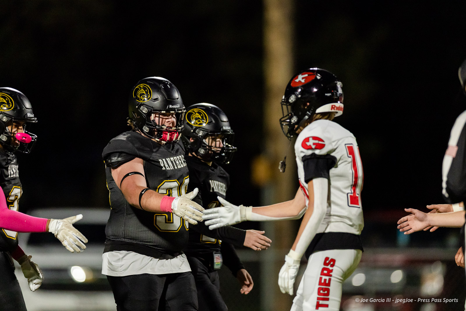 groom-vs-follett-football-jpegJoe-pps-1 | Press Pass Sports Football players in black and white uniforms shake hands after a game on a night field.