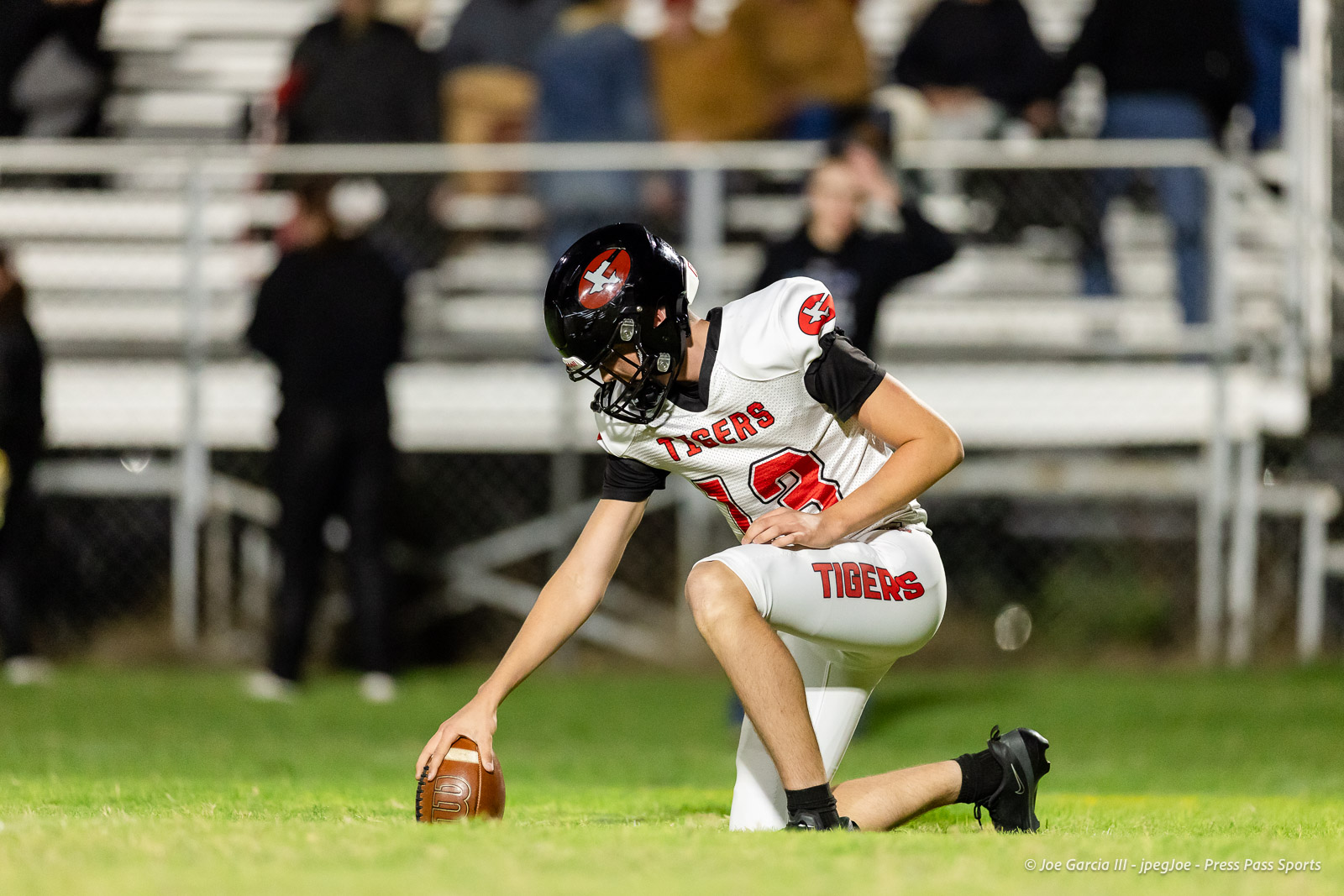 groom-vs-follett-football-jpegJoe-pps-2 | Press Pass Sports Football player in a white Tigers uniform kneels on the grass, securing the ball during a game at night.