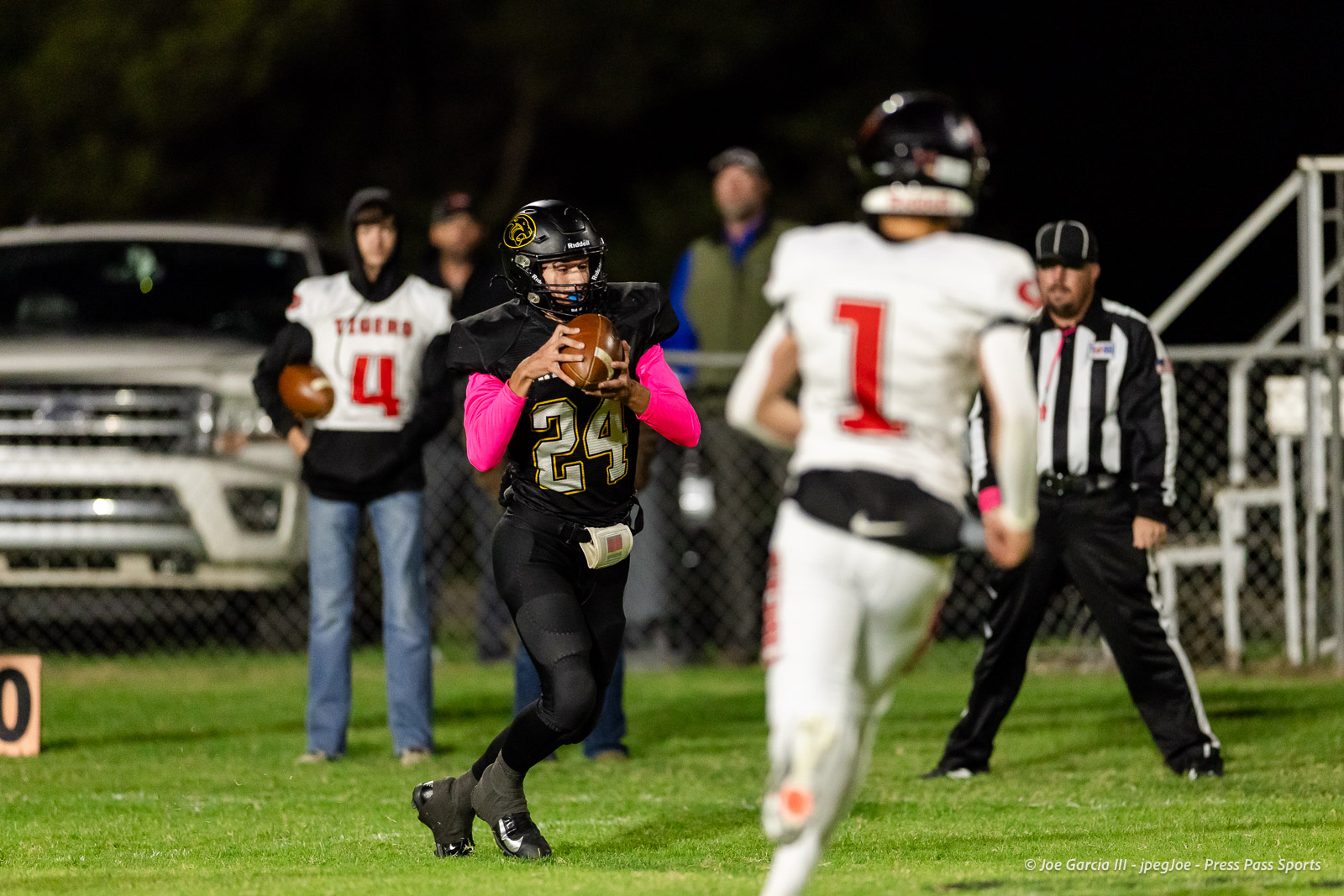 groom-vs-follett-football-jpegJoe-pps-3 | Press Pass Sports Youth football player wearing black jersey #24 with pink sleeves runs with the ball at night.