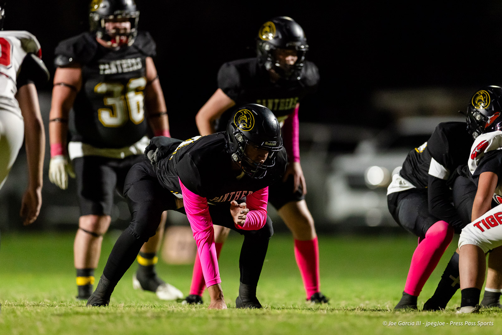 groom-vs-follett-football-jpegJoe-pps-4 | Press Pass Sports Football player in black uniform with pink sleeves crouches at the line of scrimmage during a night game, Panther logo on helmet.