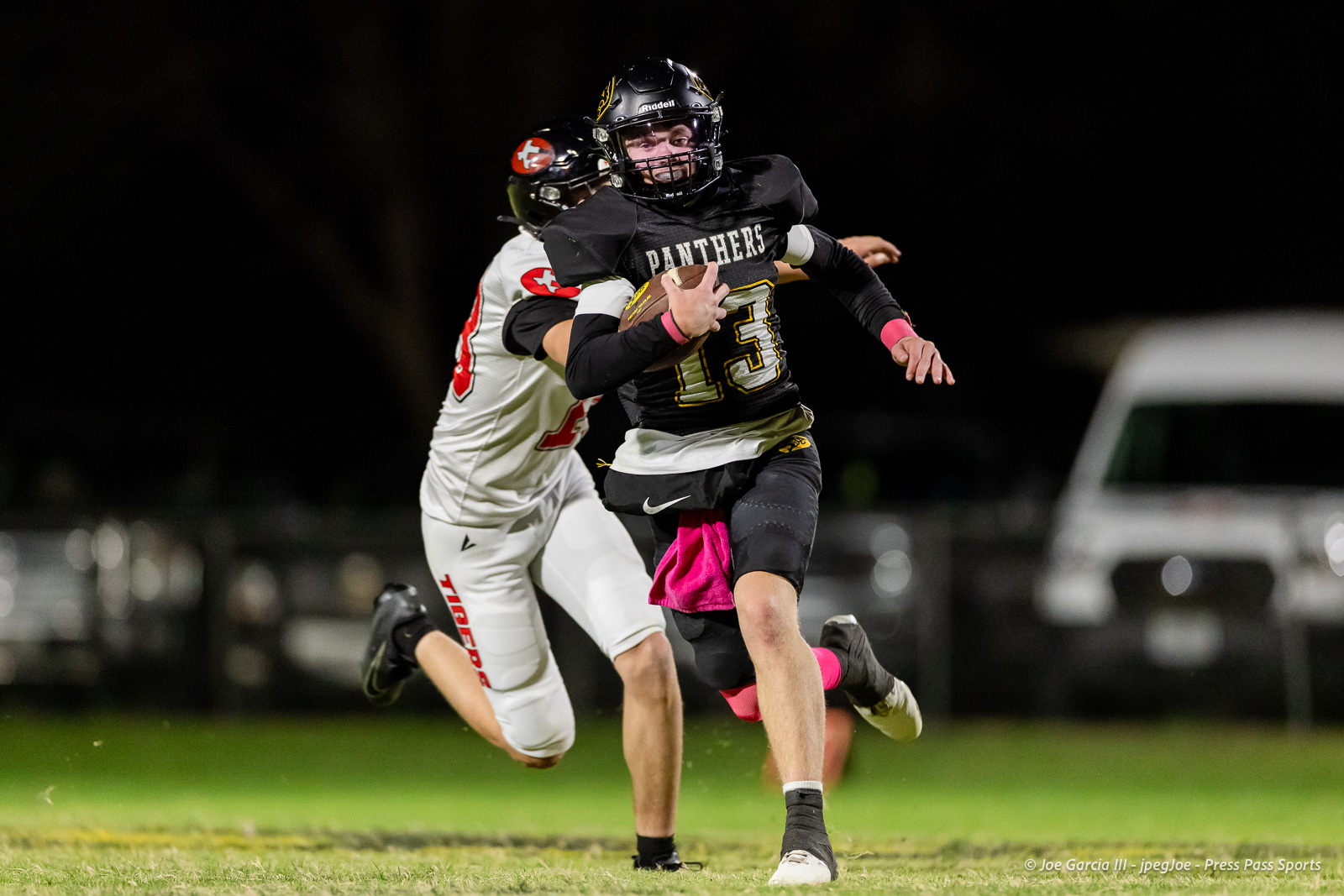 groom-vs-follett-football-jpegJoe-pps-5 | Press Pass Sports Football player in a black Panthers uniform runs with the ball, chased by a defender in white under stadium lights (night game).