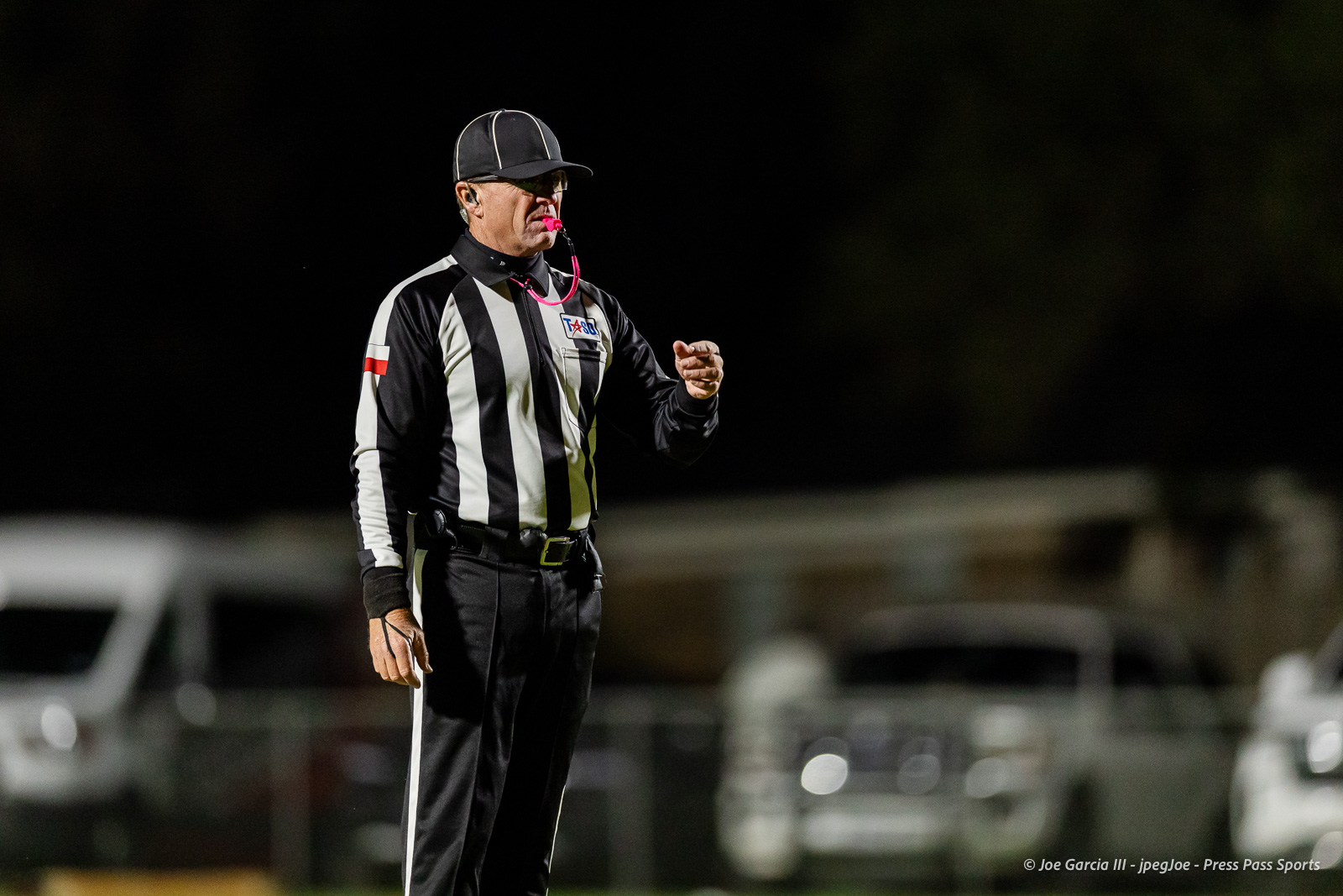 groom-vs-follett-football-jpegJoe-pps-6 | Press Pass Sports Male referee in black-and-white striped uniform whistles, standing on a field at night, gesturing with a clenched fist while wearing a cap and pink whistle lanyard.