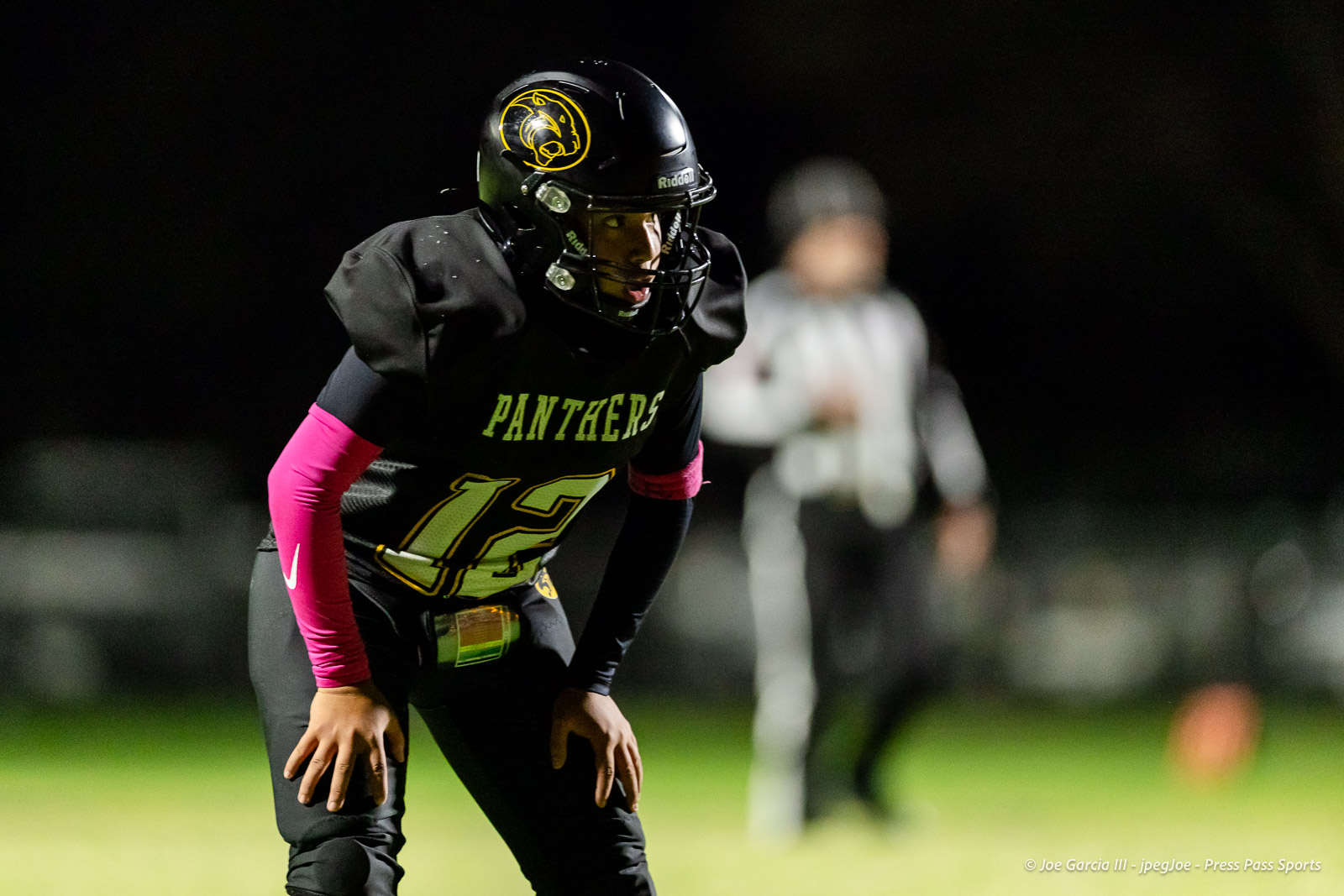 groom-vs-follett-football-jpegJoe-pps-7 | Press Pass Sports Panthers football player in a black jersey with neon green number 12, pink arm sleeves, crouched on a night field with a black helmet featuring a yellow Panthers logo.