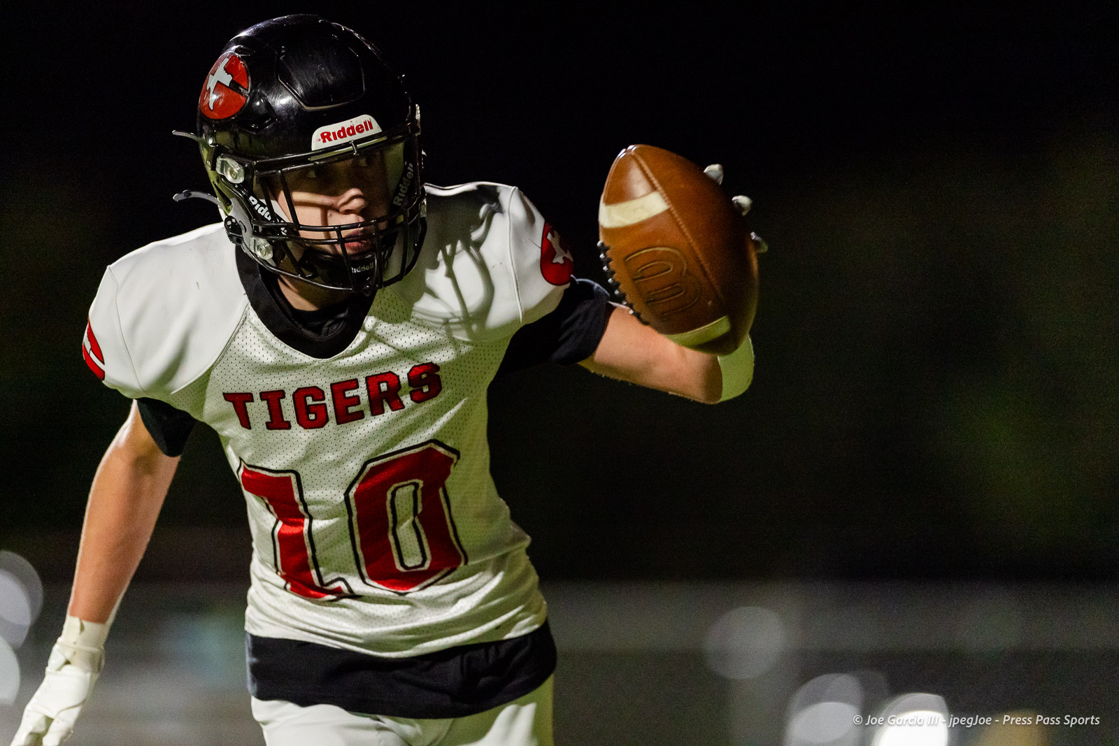 groom-vs-follett-football-jpegJoe-pps-8 | Press Pass Sports Football player in a white Tigers jersey number 10 reaches for a football during a night game, helmet on.