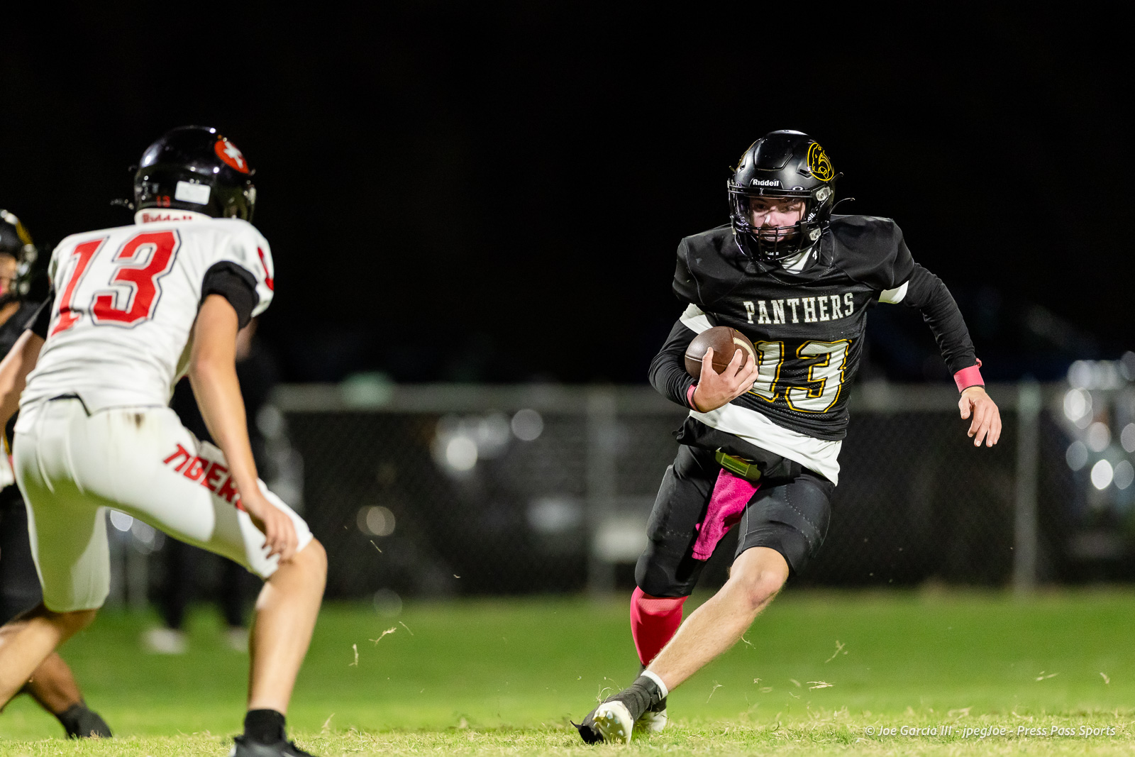 groom-vs-follett-football-jpegJoe-pps-10 | Press Pass Sports Black Panthers player wearing number 13 runs with the ball, dodging a defender in white during a night game on a grassy field.