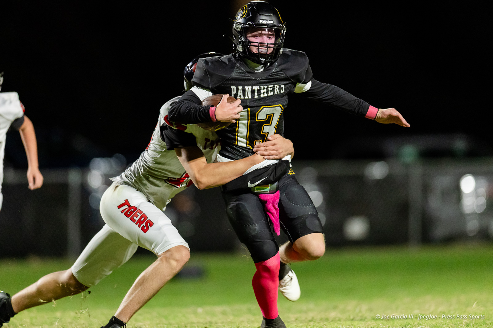 groom-vs-follett-football-jpegJoe-pps-11 | Press Pass Sports Panthers running back #13 carries the ball as a defender grips him from behind during a night game on a grassy field.