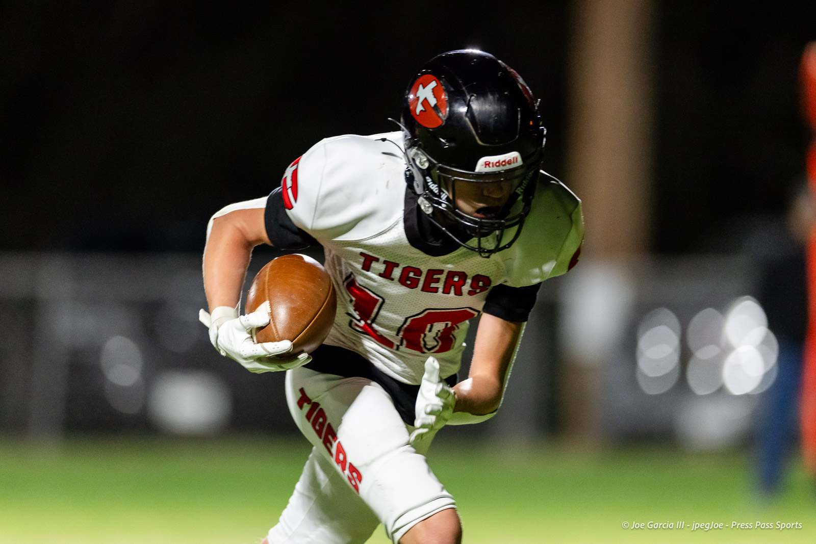 groom-vs-follett-football-jpegJoe-pps-16 | Press Pass Sports Football player in a white Tigers jersey runs with the ball at night, wearing a black helmet and white gloves.