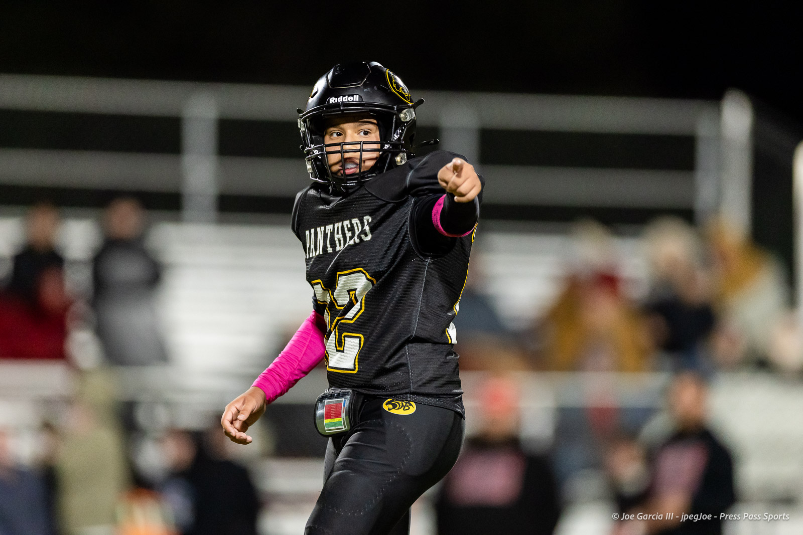 groom-vs-follett-football-jpegJoe-pps-18 | Press Pass Sports Football player in black Panthers uniform points toward the camera during a night game, wearing a helmet and pink armband on the left arm.