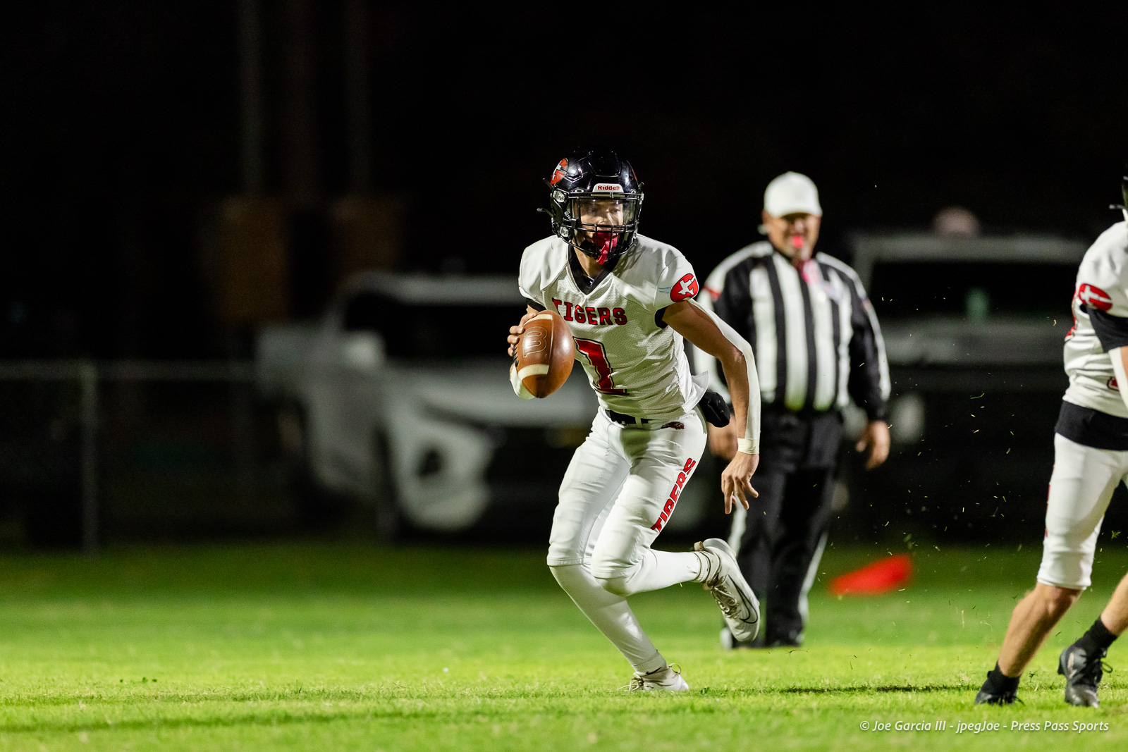 groom-vs-follett-football-jpegJoe-pps-22 | Press Pass Sports Football player in white Tigers uniform runs with the ball on a night game, a referee in the background.