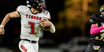 Football player in white 'Tigers' jersey runs with ball during night game, aimed forward with helmet and red number 1 visible on chest.