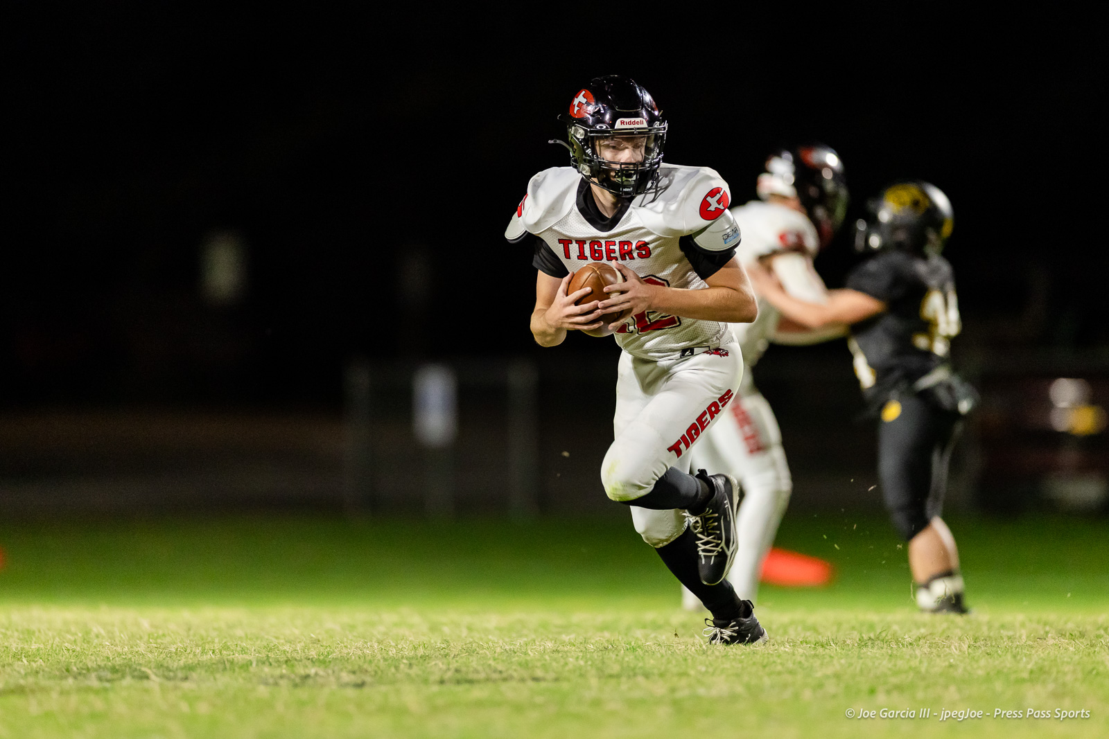 groom-vs-follett-football-jpegJoe-pps-25 | Press Pass Sports American football player in a white Tigers uniform runs with the ball during a night game, pursuing the end zone with defenders in the background.
