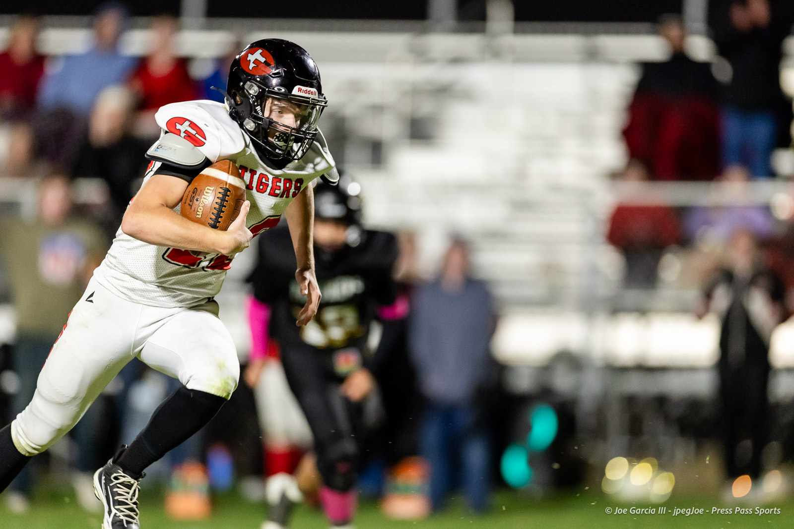 groom-vs-follett-football-jpegJoe-pps-26 | Press Pass Sports Football player in a white uniform running with the ball during a night game, stadium stands blurred in the background, tiger-themed gear visible on helmet and jersey.