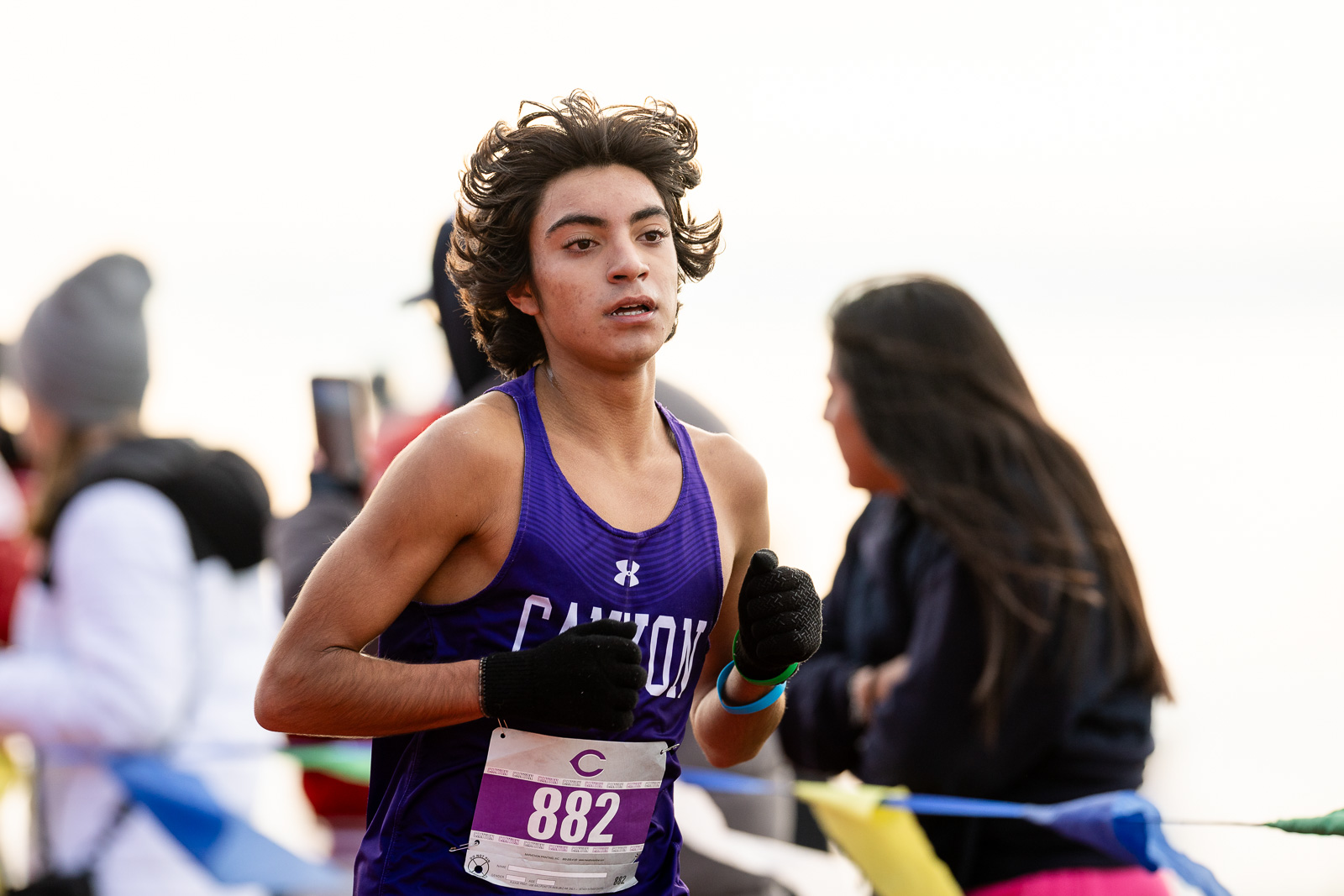 district-4a-canyon-xc-jpegJoe-pps-32 | Press Pass Sports Runner in a purple sleeveless jersey with bib 882, mid-race, hands up in gloves as spectators watch the event.