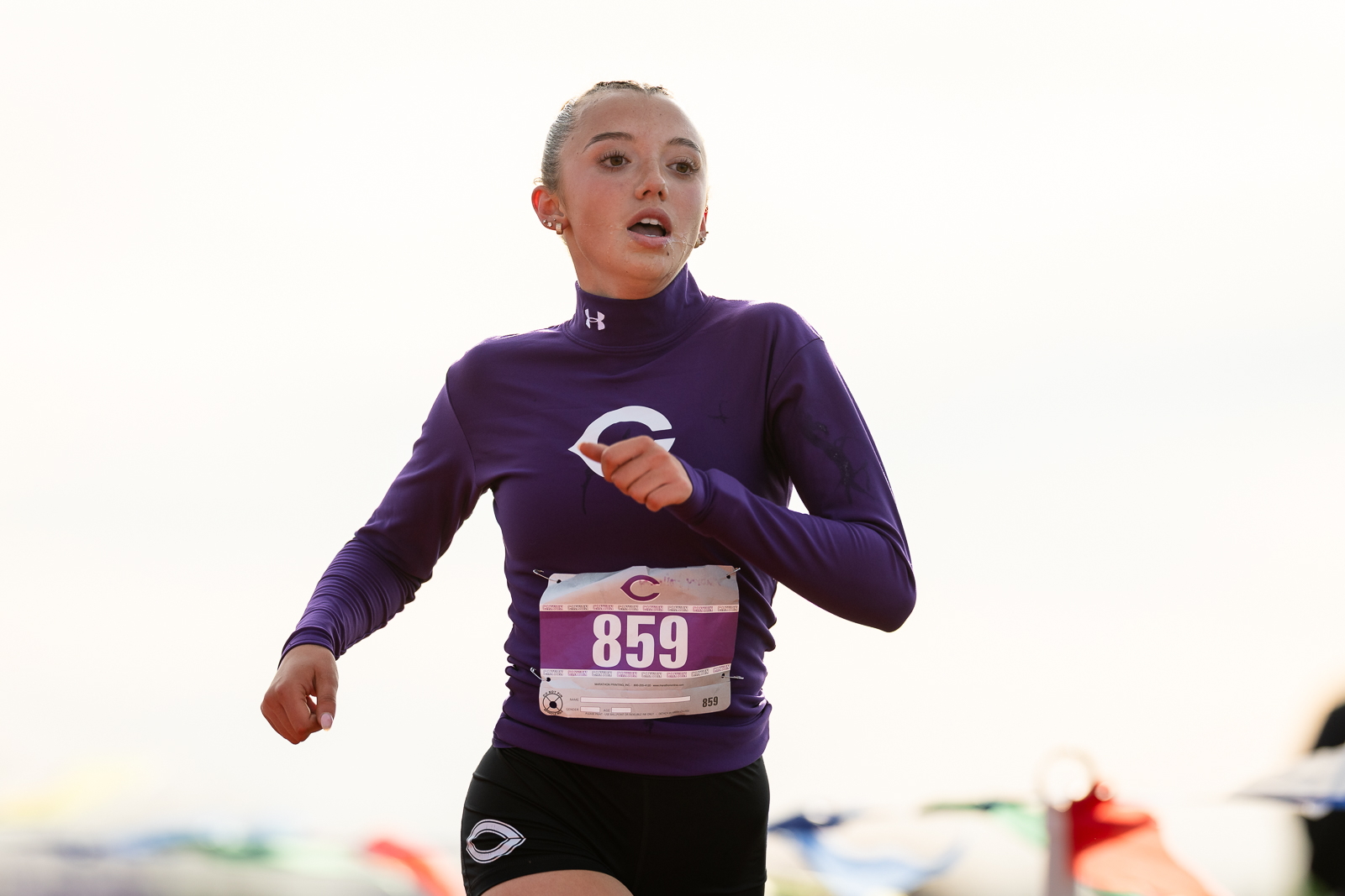 district-4a-canyon-xc-jpegJoe-pps-18 | Press Pass Sports Female runner in a purple long-sleeve top with bib 859, mid-race action against a bright sky background.