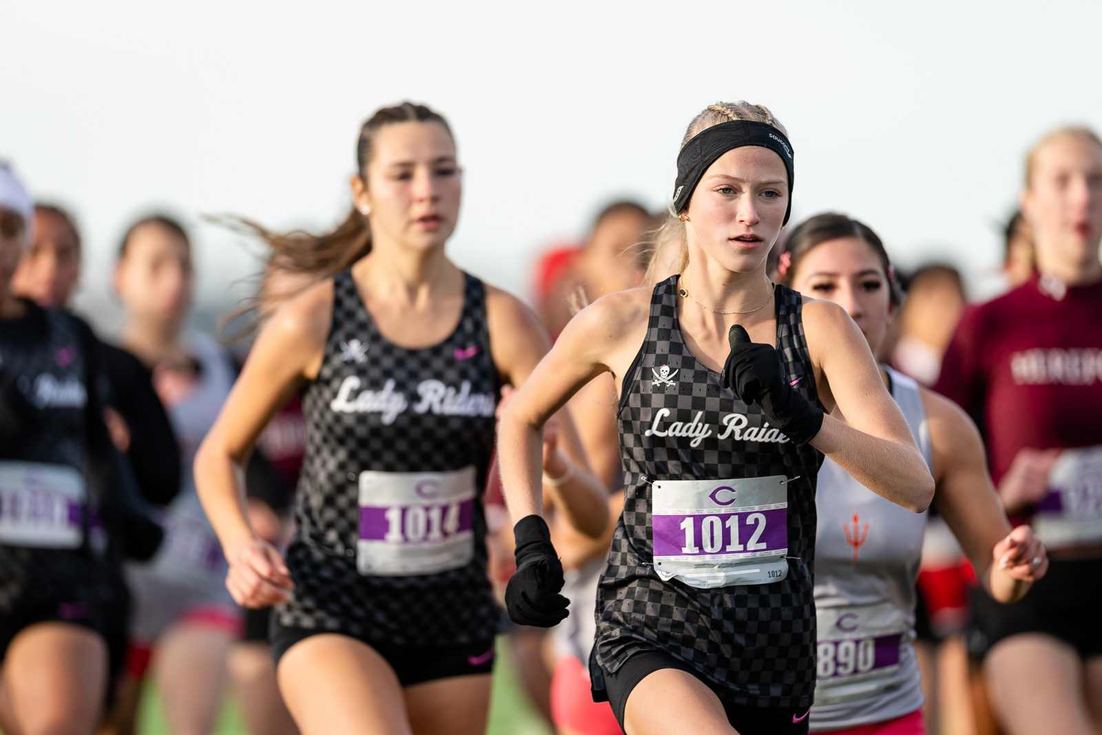 3A-4A-district-xc-jpegJoe-pps-2 | Press Pass Sports Group of female runners in a race, front center wearing a black and grey checkered top with bib 1012
