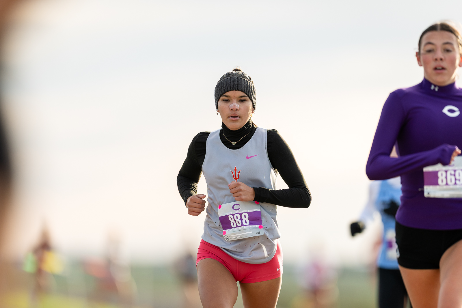 3A-4A-district-xc-jpegJoe-pps-3 | Press Pass Sports Female runner in a gray singlet, black sleeves and pink shorts, wearing a knit cap, with bib 888, mid-race.