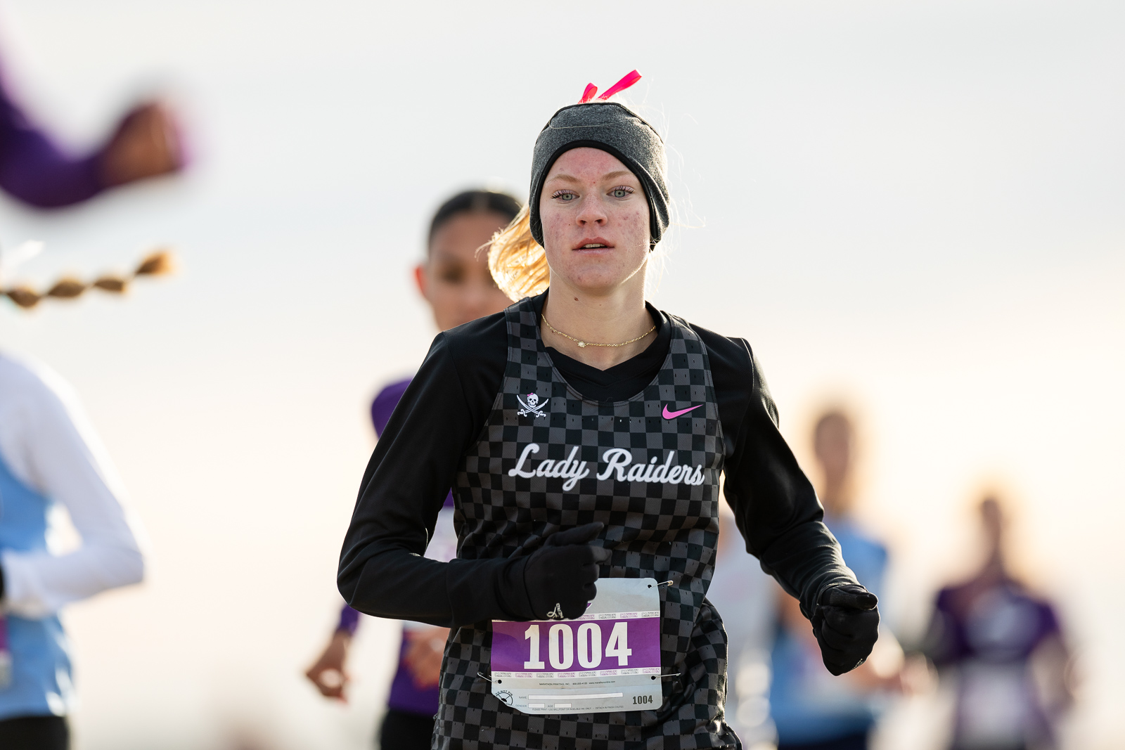 3A-4A-district-xc-jpegJoe-pps-4 | Press Pass Sports Female runner in a checkered black-and-gray jersey reading'Lady Raiders' with bib 1004, wearing a headband and gloves during a race.