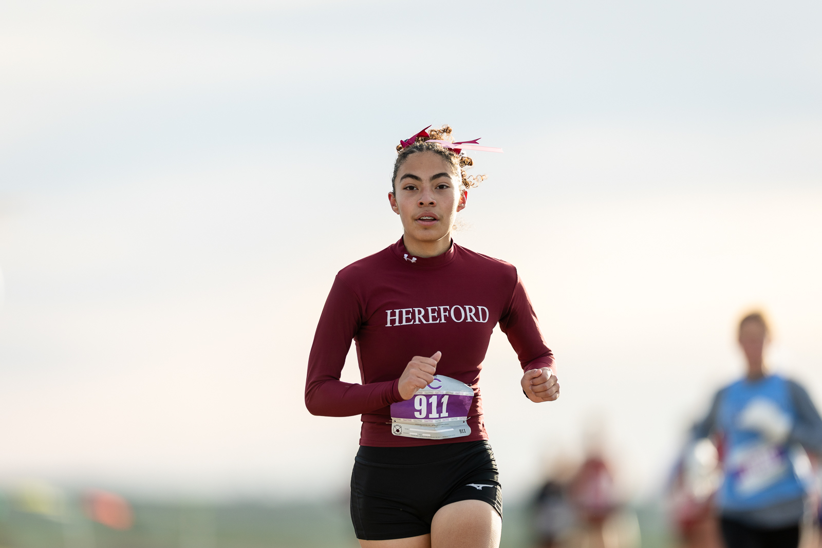 3A-4A-district-xc-jpegJoe-pps-6 | Press Pass Sports Female runner in a maroon Hereford top and black shorts, bib 911, mid-race with focused expression.