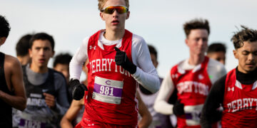 Young male runner in red and white uniform with bib 981 leading a cross-country race.