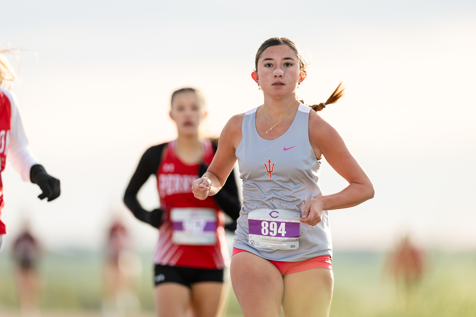3A-4A-district-xc-jpegJoe-pps-13 | Press Pass Sports Female runner in a light blue tank top and pink shorts leads a race, bib 894, with a blurred background.