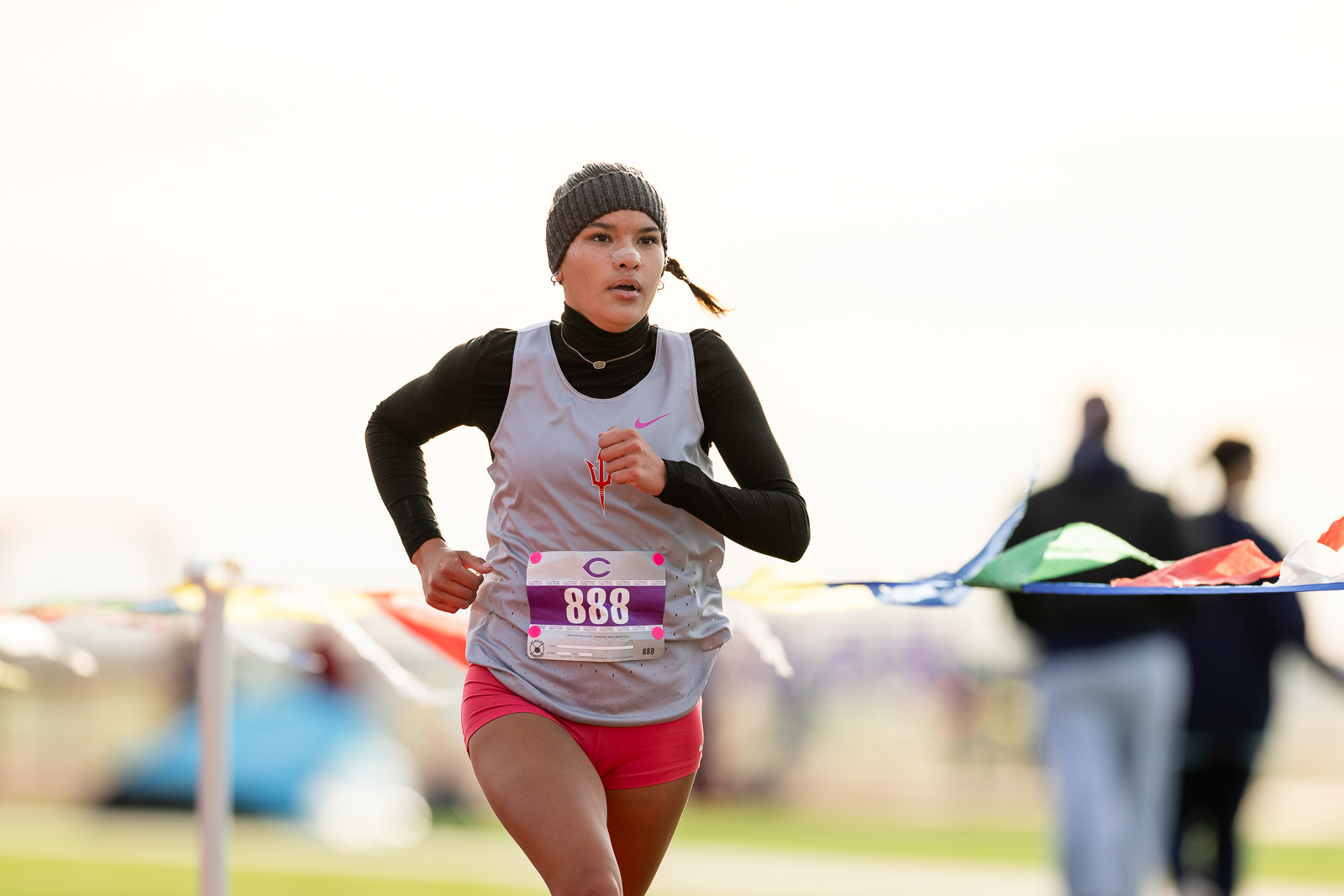 3A-4A-district-xc-jpegJoe-pps-14 | Press Pass Sports Female runner wearing a gray vest, black sleeves, pink shorts, and a knit beanie, sprinting with race bib 888 visible.
