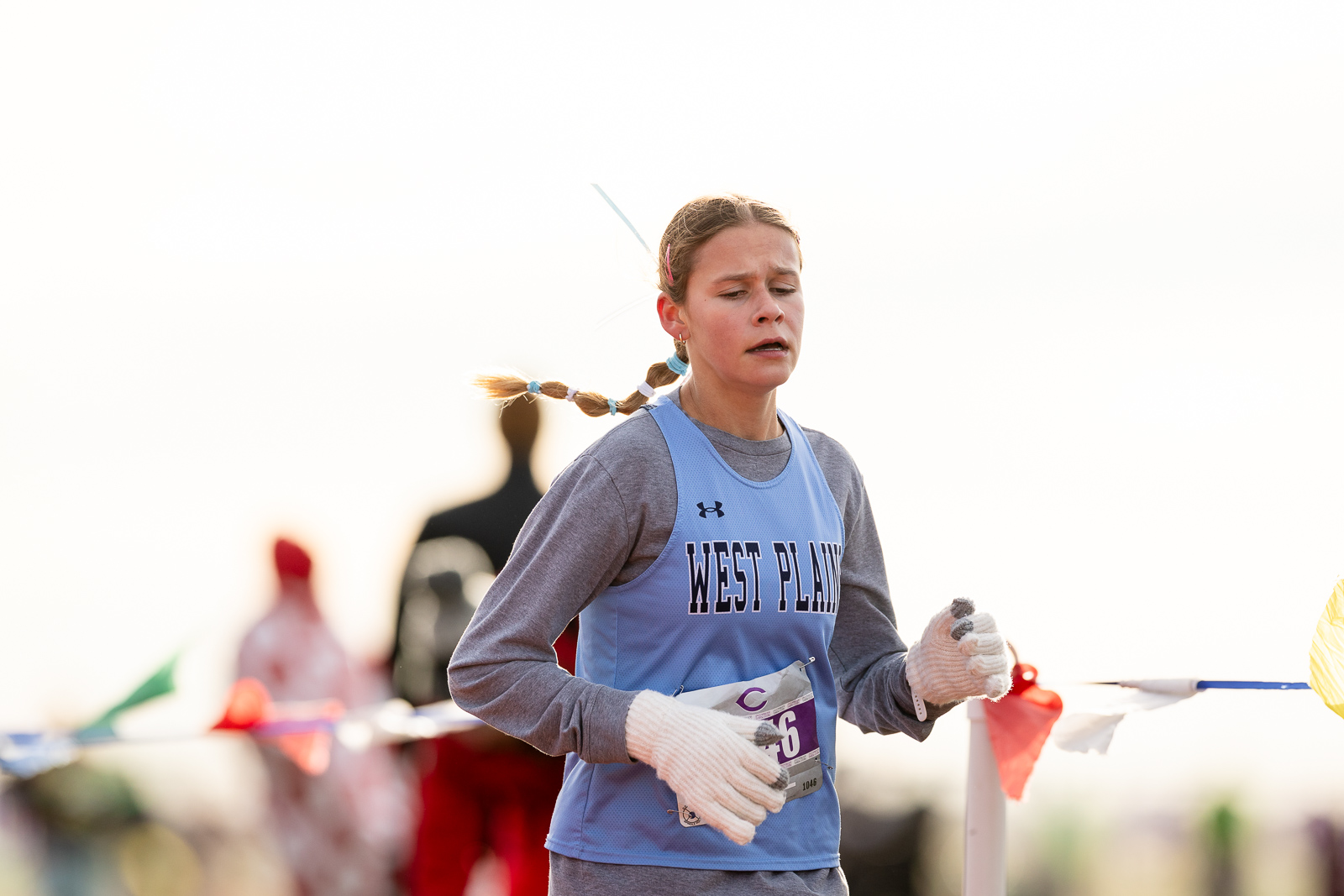 3A-4A-district-xc-jpegJoe-pps-23 | Press Pass Sports Young woman runner in a West Plains blue jersey races toward the finish line, wearing gloves and braided hair.