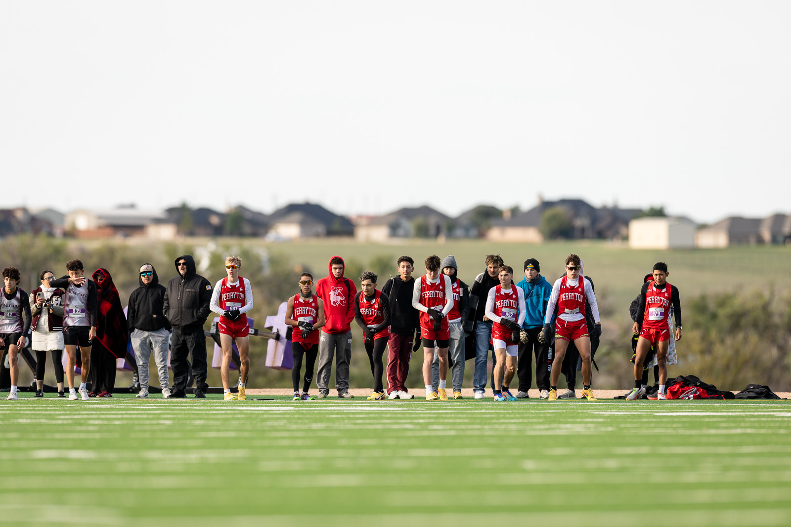 3A-4A-district-xc-jpegJoe-pps-28 | Press Pass Sports Line of runners in red and white uniforms at the track's starting line, with onlookers behind them on a sunny day.