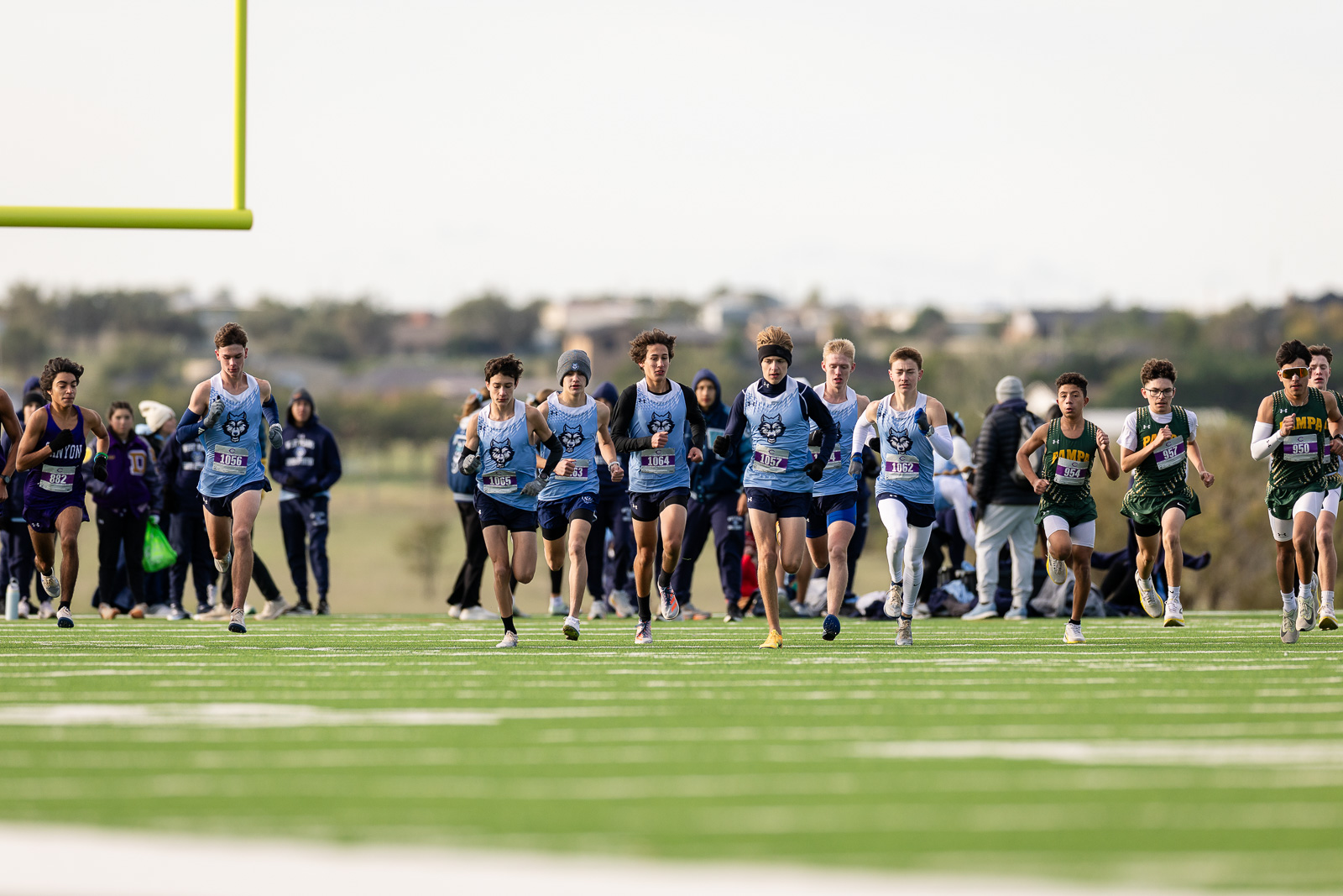 3A-4A-district-xc-jpegJoe-pps-31 | Press Pass Sports Group of runners in blue and green uniforms sprint off the starting line on a bright track, with spectators in the background.