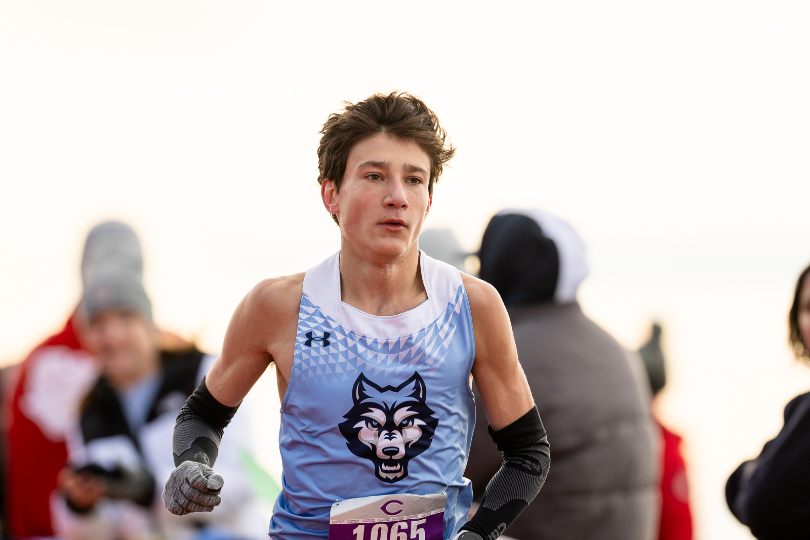 3A-4A-district-xc-jpegJoe-pps-38 | Press Pass Sports Young male runner in a light blue jersey with a wolf logo, racing outdoors, bib number 10665, focused on the track.