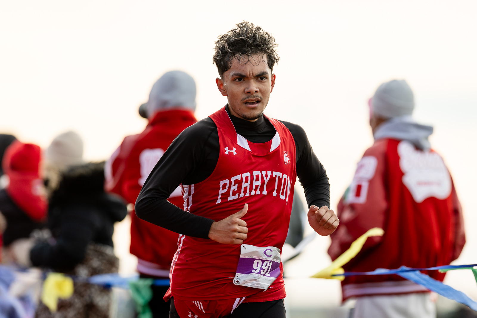 3A-4A-district-xc-jpegJoe-pps-43 | Press Pass Sports Male runner in red Perryton jersey with bib 991, racing outdoors, focused expression in mid-stride.