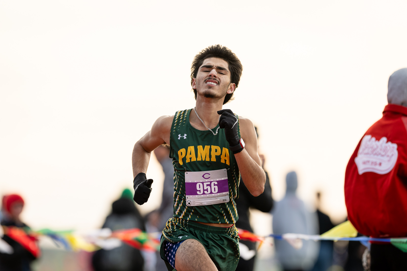 3A-4A-district-xc-jpegJoe-pps-47 | Press Pass Sports Male runner in a green and gold'PAMPA' uniform sprinting with bib number 956, mid-race on a sunlit course with spectators in the background.