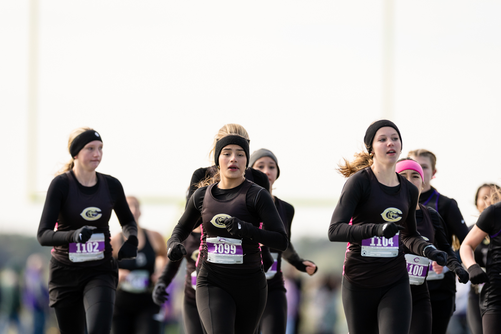 3A-4A-district-xc-jpegJoe-pps-58 | Press Pass Sports Women runners in black athletic gear with headbands, racing together on a sunny day, bib numbers visible on their waists.