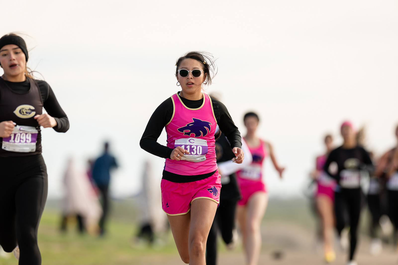 3A-4A-district-xc-jpegJoe-pps-62 | Press Pass Sports Center: woman in pink athletic outfit and sunglasses running in a race, with other runners blurred in the background.
