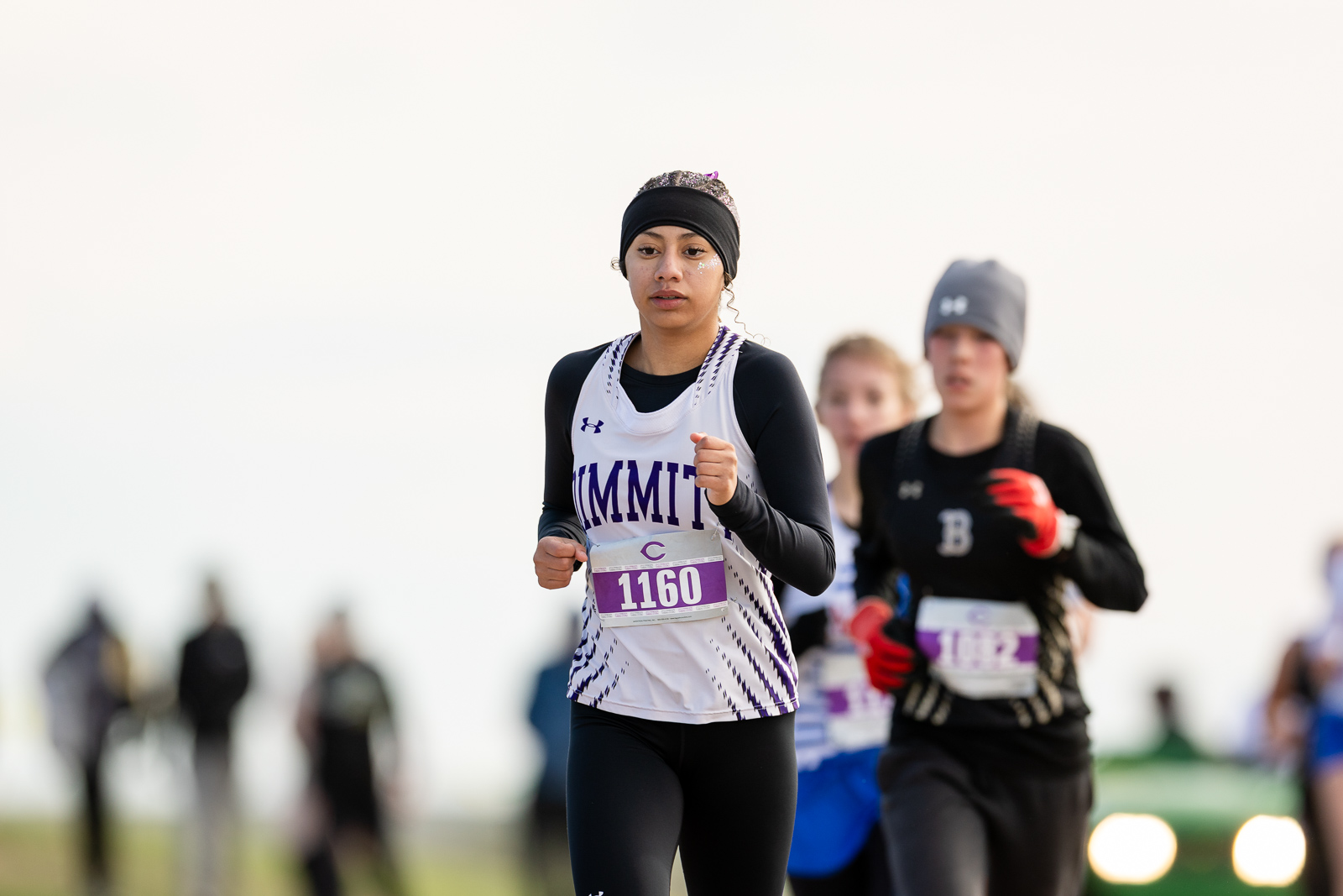 3A-4A-district-xc-jpegJoe-pps-70 | Press Pass Sports Female runner in a white purple singlet with bib 1160 leads a race, focused and mid-stride amid other runners in the background.