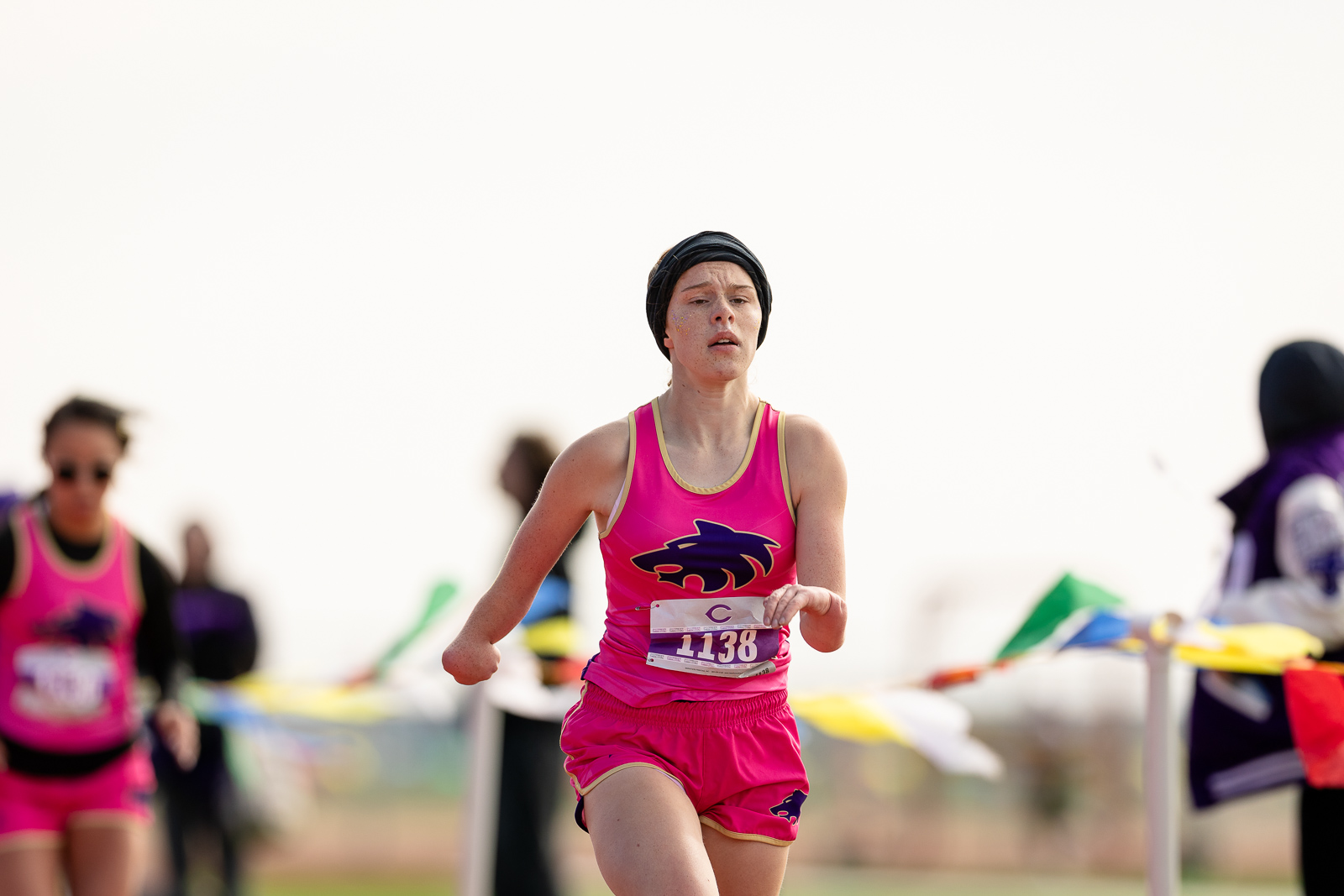 3A-4A-district-xc-jpegJoe-pps-74 | Press Pass Sports Female runner wearing a pink singlet and shorts with a black headband, mid-race with bib 1138, focused expression; blurred spectators in the background.