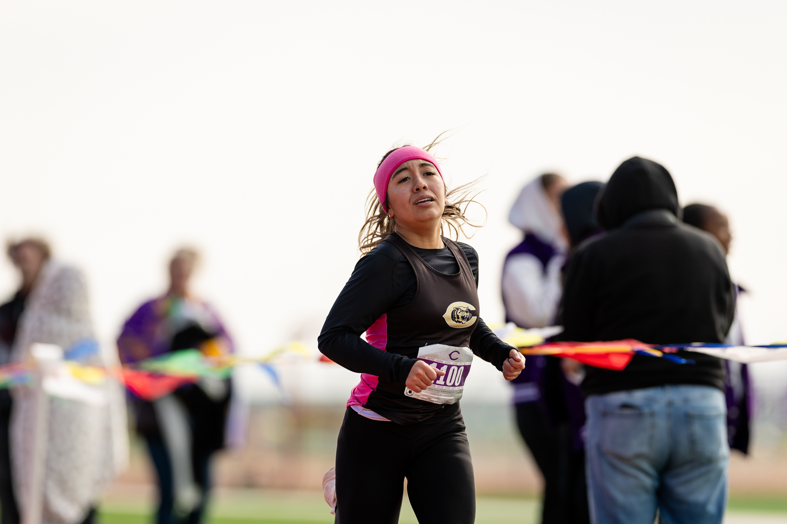 3A-4A-district-xc-jpegJoe-pps-77 | Press Pass Sports Female runner with a pink headband and black athletic attire, mid-race on a track with spectators in the background.