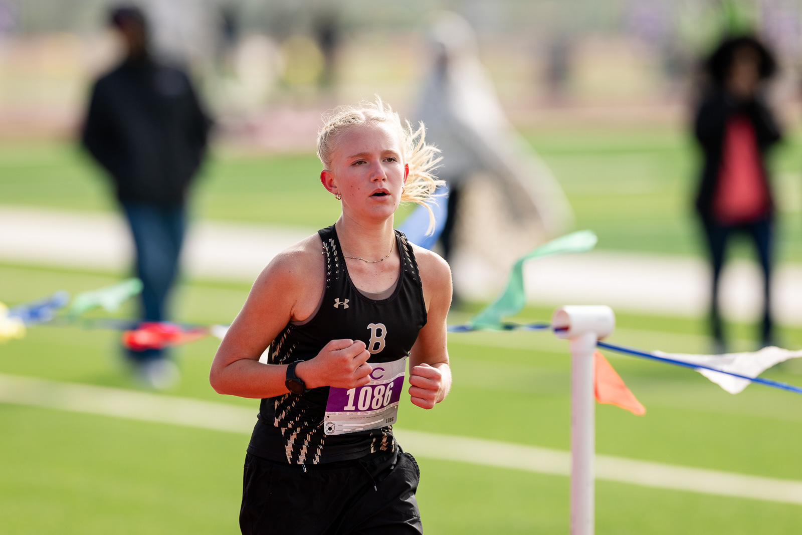 3A-4A-district-xc-jpegJoe-pps-84 | Press Pass Sports Young female athlete in a black singlet and shorts running on a track during a race, bib number 1086 visible.
