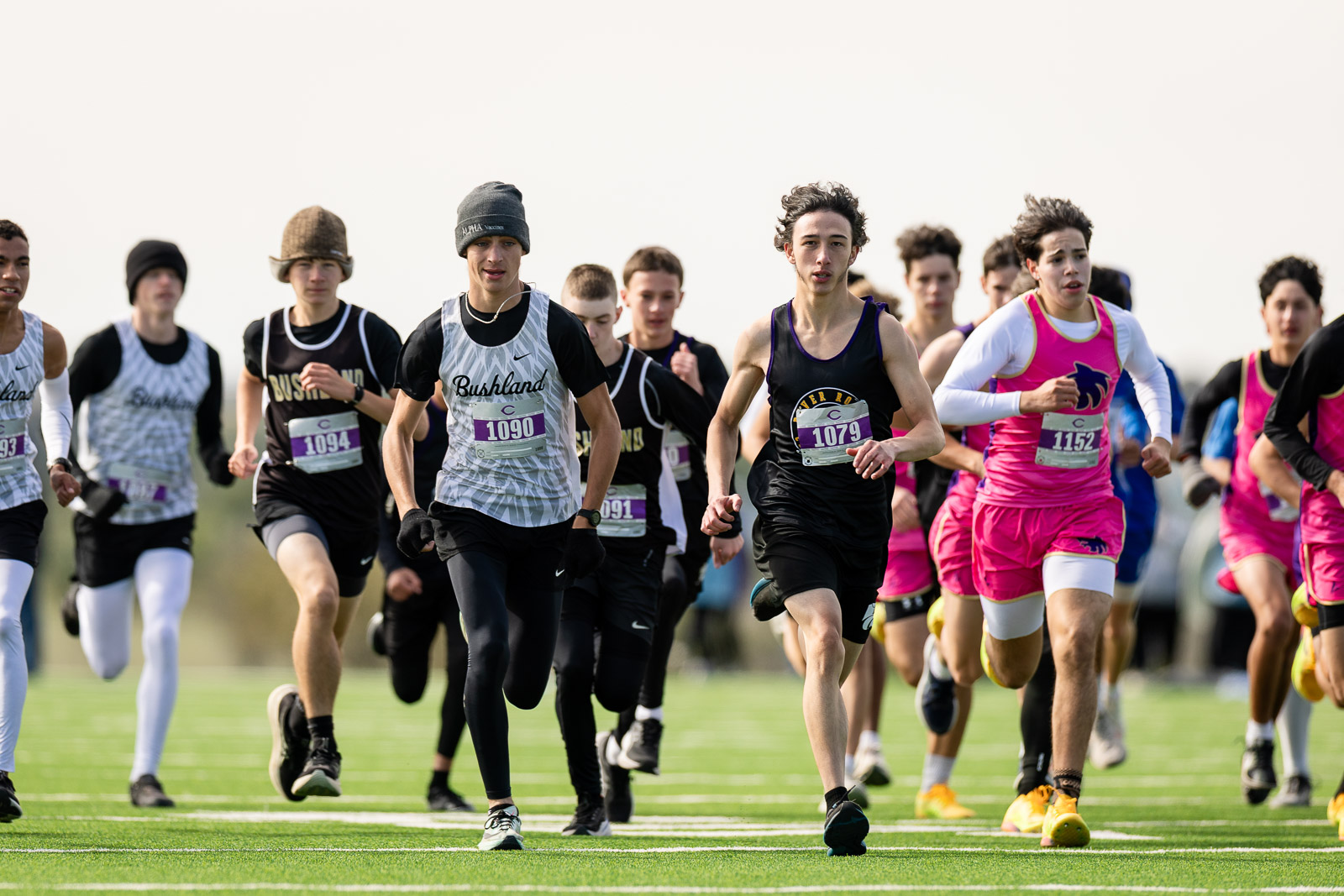 3A-4A-district-xc-jpegJoe-pps-89 | Press Pass Sports Group of runners sprinting at the start of a track race on a green field with white lane lines and numbered bibs.